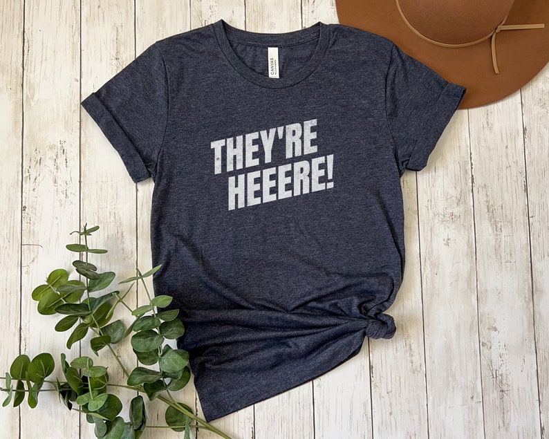 K&ouml;nnte beinhalten: Ein dunkelgraues T-Shirt mit dem Aufdruck "They're Heeeeere!" in Wei&szlig;.