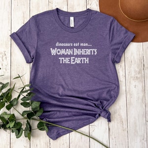 Peut inclure: T-shirt &agrave; manches courtes de couleur violette avec le texte "dinosaurs eat man... WOMAN INHERITS THE EARTH" en blanc.