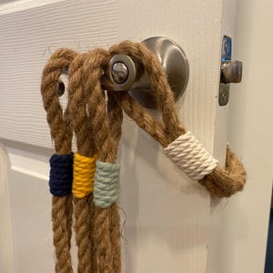 May include: Door handle rope decor with a natural brown rope and colorful accents. The rope is wrapped around the door handle and features navy blue, yellow, and light blue bands. A white band wraps the rope near the door.