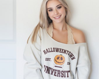 May include: A woman wearing a light gray sweatshirt with the text "Halloweentown University" and a pumpkin graphic. The sweatshirt has a brown and white color scheme.