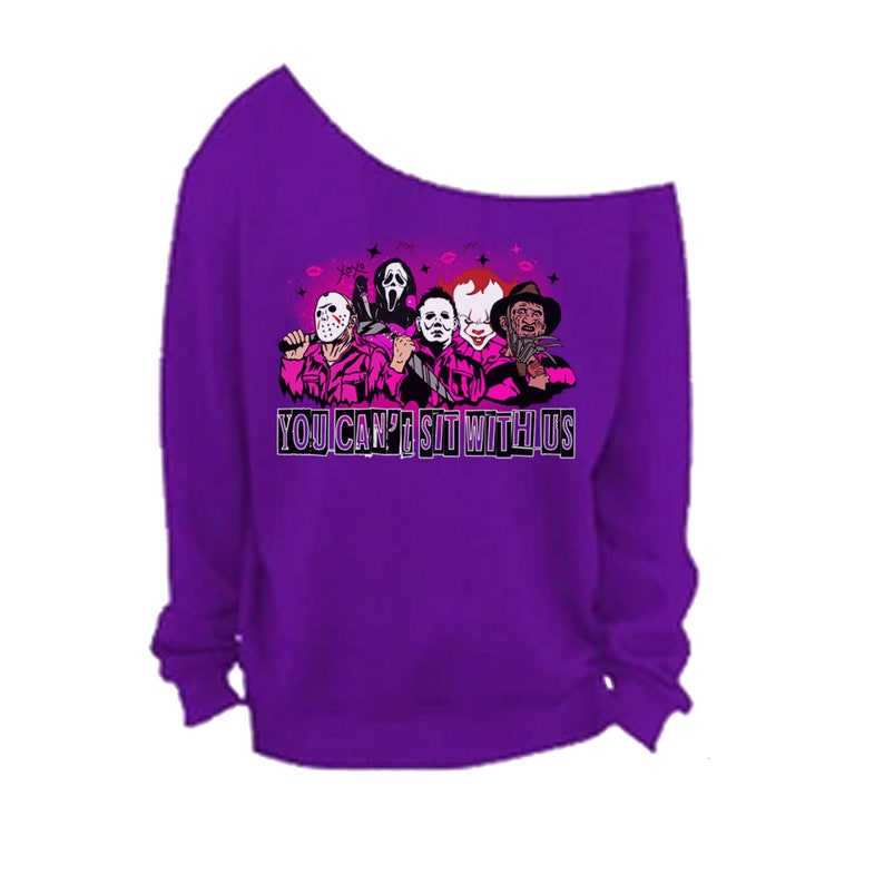 May include: Purple off-the-shoulder sweatshirt with a graphic of horror movie characters and the text "You Can't Sit With Us".