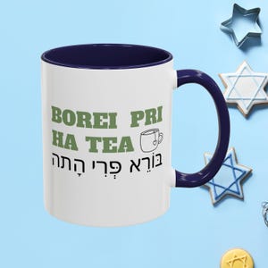May include: White ceramic mug with a navy blue rim and handle. The mug has the text "BOREI PRI HA TEA" in green letters and a small green teacup icon. The text "בּוֹרֵא פְּרִי הַתֵּא" is in Hebrew below the English text.