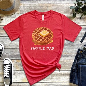 K&ouml;nnte beinhalten: Rotes T-Shirt mit kurzen &Auml;rmeln, einem Waffel- und Butter-Motiv und dem Text "Waffle Dad".