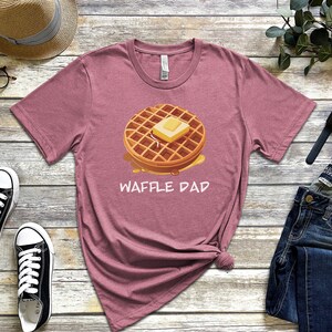 K&ouml;nnte beinhalten: Ein heidefarbenes T-Shirt mit einem Aufdruck einer Waffel mit Butter und Sirup. Der Text "Waffle Dad" ist unter der Waffel aufgedruckt.