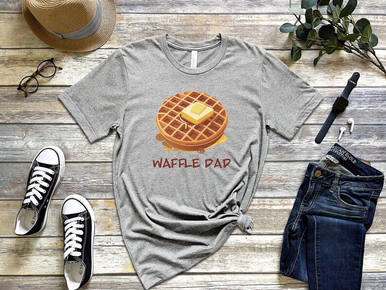 K&ouml;nnte beinhalten: Ein graues T-Shirt mit einem Cartoon-Waffel mit Butter und Sirup. Der Text "Waffle Dad" ist unter der Waffel gedruckt.