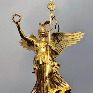 Könnte beinhalten: Eine goldene Statue einer geflügelten Figur, die einen Stab mit einem Kreuz und einem Kranz hält. Die Statue steht auf einem Sockel und ist vor einem grauen Himmel platziert.