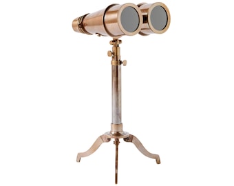 May include: A brass nautical binocular set mounted on a matching brass tripod stand. The binoculars feature two circular lenses with dark glass, connected to a central vertical post with adjustable knobs for height and focus, supported by three legs.