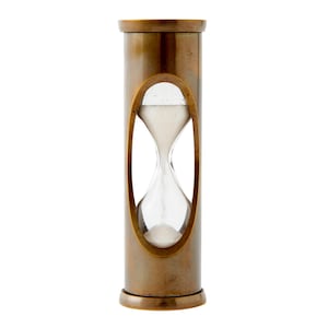 May include: A cylindrical hourglass featuring a weathered brass frame with a smooth, polished finish. The central section contains a clear glass bulb filled with fine white sand, visible through an oval cutout in the metal casing.