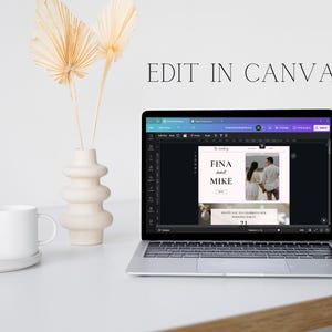 May include: A laptop displaying a wedding invitation design with the text "FINA and MIKE" and "INVITE YOU TO CELEBRATE OUR WEDDING PARTY 21". The screen is open on a white desk next to a white mug, a decorative vase, and dried palm leaves. The text "EDIT IN CANVA" is above the laptop.