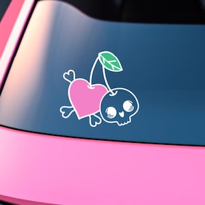 Op de afbeelding: Een witte vinyl sticker met een roze hart en een zwarte schedel. Het hart en de schedel zijn verbonden door een groene steel met een blad. De sticker is ontworpen om op een kers te lijken.