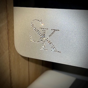 Op de afbeelding: Een close-up van een zilveren oppervlak met de letters "SK" gespeld in strass.