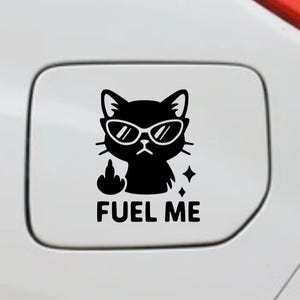 May include: Black cat graphic wearing sunglasses, giving the middle finger, with the text "FUEL ME". The sticker is applied to a white surface.