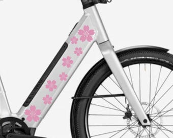 Könnte beinhalten: Ein weißes Elektrofahrrad mit pinkfarbenen Kirschblüten-Aufklebern am Rahmen. Das Fahrrad hat einen schwarzen Sattel, einen schwarzen Lenker und schwarze Räder.