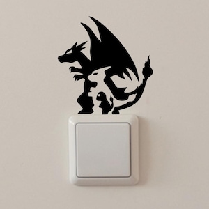 Peut inclure: Autocollant mural en silhouette noire et blanche de trois personnages Pokémon, Charizard, Charmeleon et Charmander, sur un mur blanc à côté d'un interrupteur.