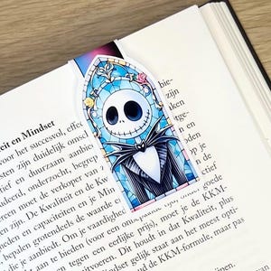 Op de afbeelding: Een blauwe en zwarte bladwijzer met een cartoonfiguur met een wit gezicht en zwarte ogen. Het personage draagt een zwart pak en een zwarte vlinderdas. De bladwijzer is gevormd als een glas-in-loodraam.