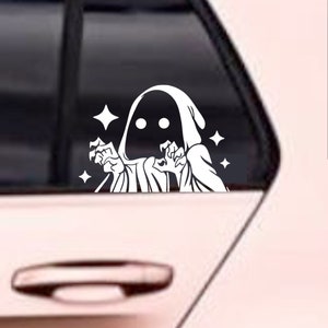 May include: White vinyl sticker of a hooded figure with glowing stars, appearing to be reaching out with its hands.