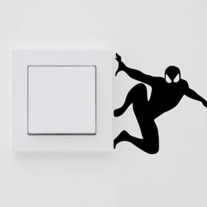 May include: Black silhouette of a superhero figure, possibly Spiderman, climbing up a white light switch plate.