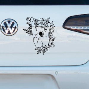 Puede incluir: Pegatina en blanco y negro de arte de línea de una mano haciendo el gesto de rock and roll con flores que la rodean.
