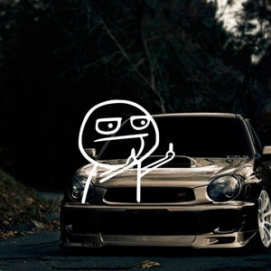 May include: A black Subaru Impreza WRX with a white stick figure giving the middle finger. The car is parked in a dark forest setting.