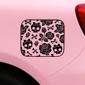 May include: A pink car featuring a black and white design on the fuel filler flap. The design is a pattern of skulls with bows, roses, and crossbones. The car's bodywork is a light pink colour.