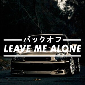 Op de afbeelding: Een zwarte Subaru Impreza met de tekst "Leave Me Alone" in witte letters op een zwart-witte banner boven de auto. De tekst "バックオフ" is in het Japans boven de banner.
