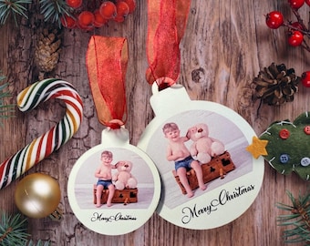 May include: Two white Christmas ornaments with a photo of a child and a teddy bear, with the words "Merry Christmas" in script. The ornaments hang from red ribbons. The background includes a candy cane, pine needles, and berries.