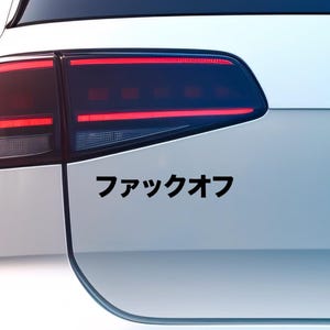Op de afbeelding: Een witte auto met een zwarte sticker waarop in Japanse karakters "ファックオフ" staat.