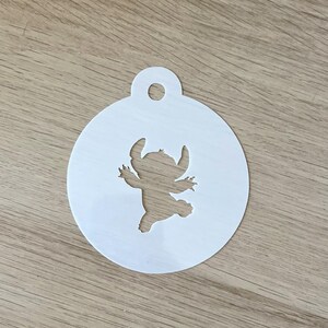 May include: White plastic stencil featuring a silhouette of Stitch from Lilo & Stitch. The stencil has a hole at the top for hanging.