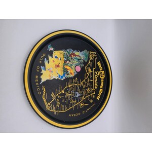 May include: A round black serving tray with a yellow rim featuring a colorful map of Florida and Walt Disney World. The graphic includes illustrations of Disney characters, the Gulf of Mexico, the Atlantic Ocean, and various Florida landmarks.