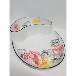May include: White ceramic serving dish with a black rim and a unique two-section design. The dish is decorated with colorful travel-themed stamps and text, including the words "Central America" and "Mexico".