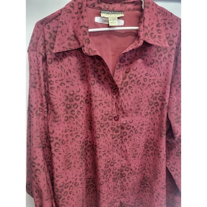 May include: A burgundy button-down shirt with a leopard print pattern. The shirt has long sleeves, a collared neckline, and a button closure. The brand name "NOTATIONS CLOTHING CO." is visible on the label.