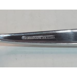 May include: Close-up of a stainless steel utensil with the text "© WATERFORD E.D. STAINLESS" etched into the metal. The utensil has a reflective surface and is set against a plain background.