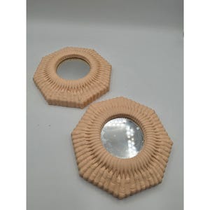 May include: Two hexagonal mirrors featuring light peach-colored frames with a textured, ribbed, and radiating pattern surrounding the circular glass centers. The frames have a matte finish and a geometric shape with six distinct sides.