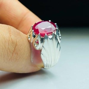 Peut inclure: Une bague en argent avec une grande pierre précieuse de rubis de forme ovale. La bague a un design détaillé et orné.