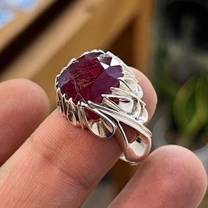 May include: A silver ring with a large, red gemstone set in a detailed, ornate design.