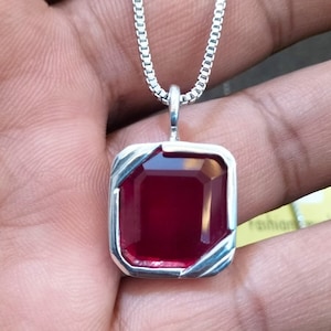 May include: A silver chain necklace with a red gemstone pendant. The pendant is a square with a beveled edge and a shiny, red gemstone in the center.