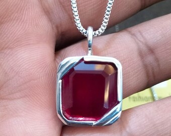 May include: A silver chain necklace with a red gemstone pendant. The pendant is a square with a beveled edge and a shiny, red gemstone in the center.