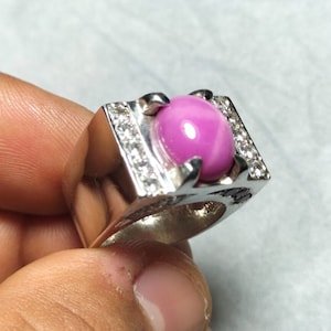 Puede incluir: Un anillo de plata con una piedra preciosa de zafiro estrella rosa rodeada de pequeñas piedras preciosas transparentes.