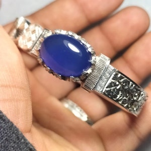 Puede incluir: Una pulsera de plata con un diseño intrincado y una gran piedra preciosa azul de forma ovalada.