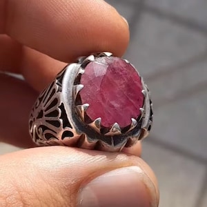 Puede incluir: Un anillo de plata con un diseño adornado y una gran piedra preciosa de rubí rosa de forma ovalada.