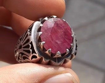 May include: A silver ring with an ornate design and a large, oval-shaped, pink ruby gemstone.