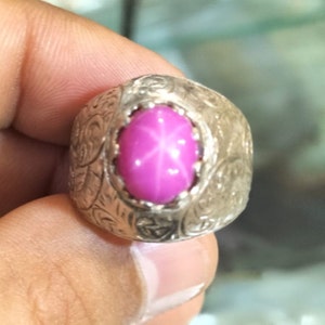 Puede incluir: Un anillo de plata con un diseño adornado y una piedra preciosa de zafiro estrellado rosa.