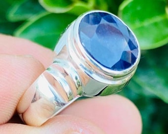 May include: A silver ring with a large, oval-cut, dark blue gemstone. The ring has a polished, metallic band with a simple, elegant design. The gemstone is faceted, reflecting light and adding a touch of luxury.