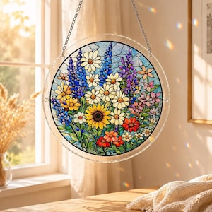 May include: A round, stained glass window hanging featuring a colorful floral design. The artwork includes a sunflower, daisies, and other flowers in shades of yellow, blue, purple, and red. The glass is framed by a clear, circular border and suspended by a chain.