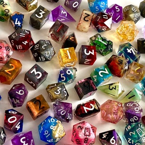 May include: A collection of colourful, multi-sided dice with various numbers and patterns. The dice are made of clear resin with embedded glitter and other decorative elements.