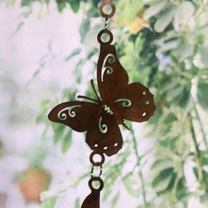May include: A metal butterfly wind chime with a rusty brown finish. The butterfly is hanging from a chain with other butterflies below it.