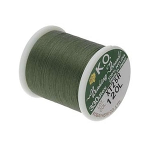 May include: A spool of olive green K.O. Beading Thread made of 100% nylon. The white label on the side displays the text K.O. Beading Thread, 330dtex, XT25R, 120L, 100% Nylon, Made in Japan, and Kobayashi Co., Ltd. The thread is wound tightly.