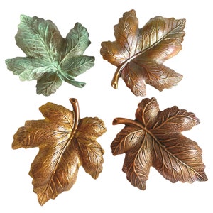 Op de afbeelding: Vier decoratieve metalen schalen in de vorm van een blad. Twee zijn lichtgroen en twee zijn goudkleurig.