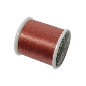 May include: A spool of copper-colored thread wound tightly around a white plastic core. The end of the spool features a dark green label with white text that reads KO and includes additional small printed details on the circular surface.