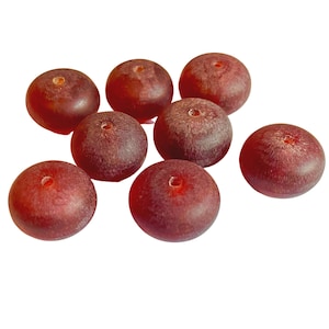 May include: A collection of seven round, dark red beads with a smooth, slightly translucent finish. Each bead features a central hole, displaying a consistent spherical shape and a deep, uniform maroon color throughout the entire set of items.